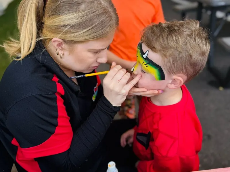 A face painter painting a child's face at the festival, with another painted child behind